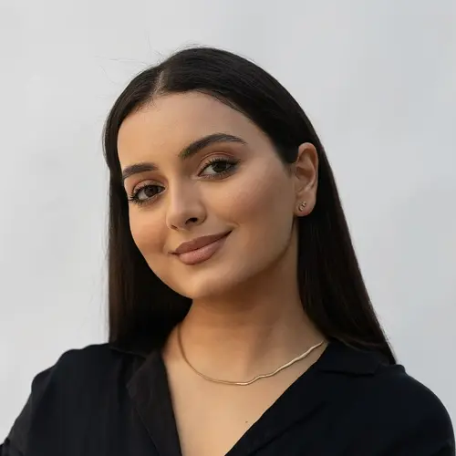 Frau mit langen, dunklen Haaren und einem schlichten Halsband, lächelt in die Kamera.